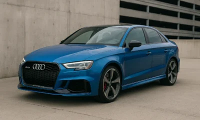 Audi RS3 bleue garée devant un mur en béton dans un décor urbain