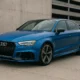 Audi RS3 bleue garée devant un mur en béton dans un décor urbain