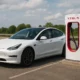 Une Tesla Model 3 blanche en train de se recharger sur une borne Superchargeur Tesla en bord d'autoroute