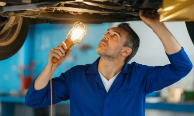 Mécanicien inspectant le dessous d’une voiture avec une lampe, illustrant les risques de rouler sans contrôle technique