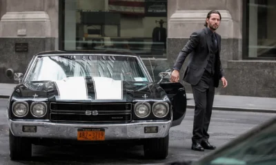 John Wick en costume noir sortant d’une Chevrolet Chevelle SS classique noire avec bandes blanches