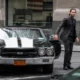 John Wick : quand les muscle cars racontent l'histoire John Wick en costume noir sortant d’une Chevrolet Chevelle SS classique noire avec bandes blanches